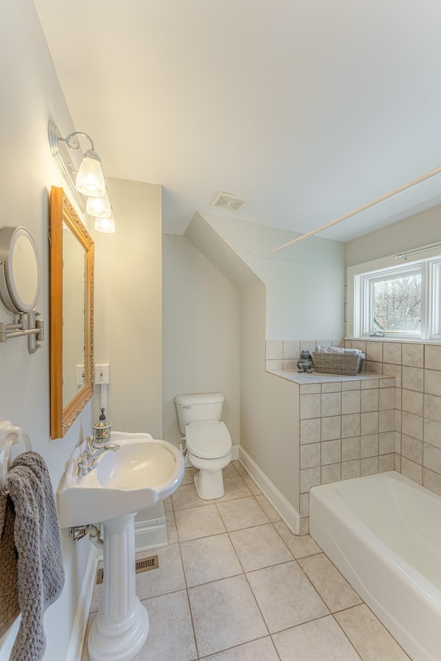 bathroom with tile patterned flooring, visible vents, baseboards, toilet, and a tub to relax in