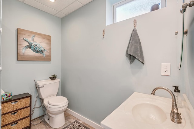 bathroom featuring a drop ceiling, toilet, sink, and tile patterned floors