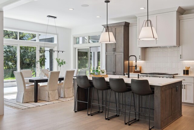 kitchen with pendant lighting, tasteful backsplash, light hardwood / wood-style flooring, and a center island with sink