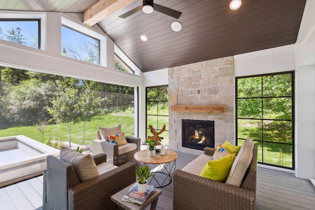 sunroom / solarium featuring a healthy amount of sunlight, ceiling fan, a fireplace, and vaulted ceiling with beams