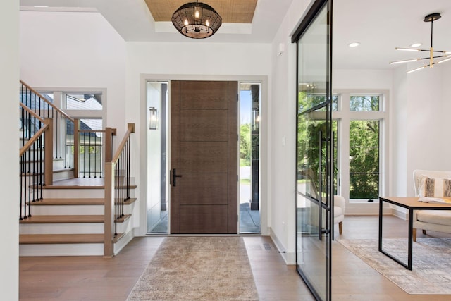 entrance foyer with light hardwood / wood-style flooring, a tray ceiling, and a chandelier