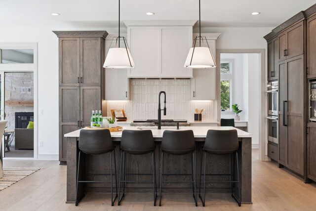 kitchen featuring a kitchen breakfast bar, light hardwood / wood-style flooring, an island with sink, hanging light fixtures, and decorative backsplash