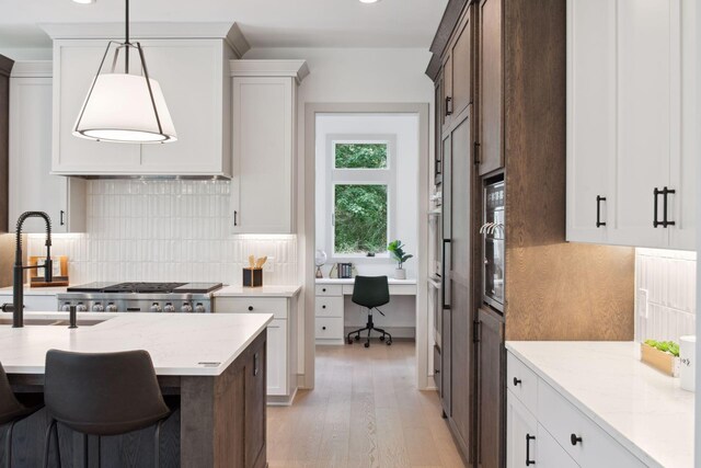 kitchen featuring light wood-type flooring, pendant lighting, backsplash, light stone counters, and sink