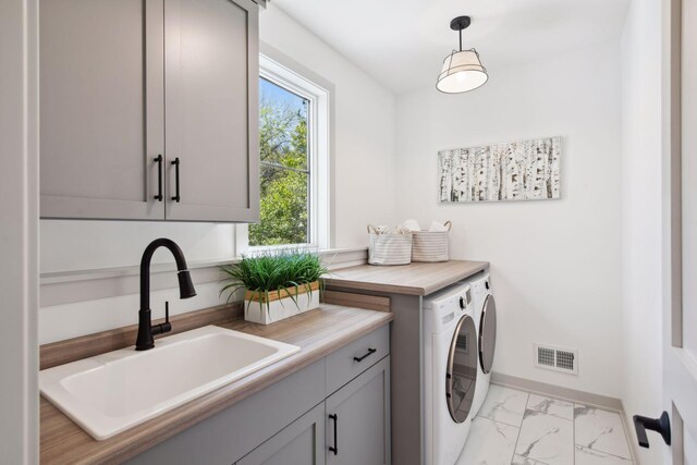 clothes washing area with cabinets, washing machine and dryer, and sink