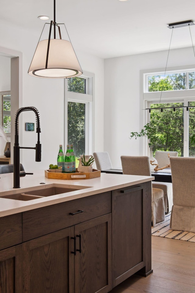 kitchen with hanging light fixtures, dark brown cabinets, sink, and light hardwood / wood-style floors