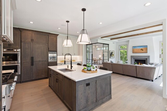 kitchen featuring beamed ceiling, decorative light fixtures, an island with sink, sink, and light hardwood / wood-style floors