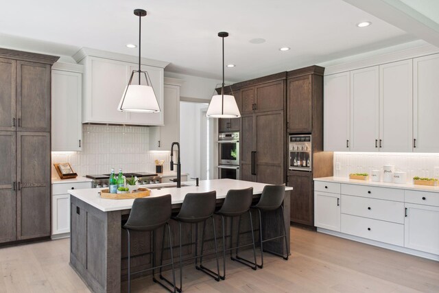 kitchen with an island with sink, light hardwood / wood-style flooring, a kitchen breakfast bar, and tasteful backsplash