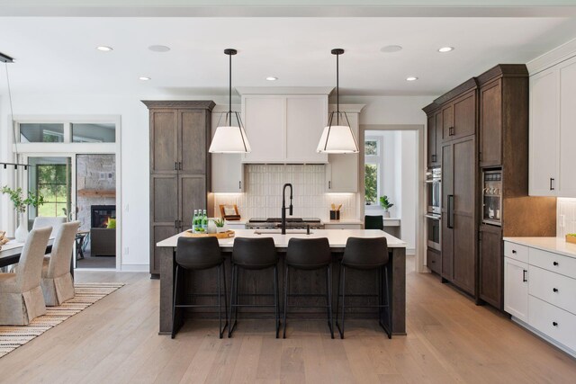 kitchen with light wood-type flooring, a kitchen island with sink, and a healthy amount of sunlight