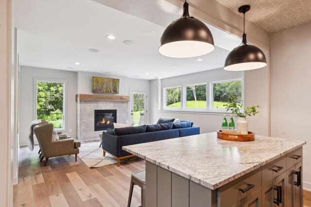 kitchen featuring a fireplace, pendant lighting, a healthy amount of sunlight, and light hardwood / wood-style floors