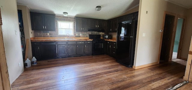 kitchen featuring decorative backsplash, dark wood-type flooring, under cabinet range hood, black appliances, and a sink