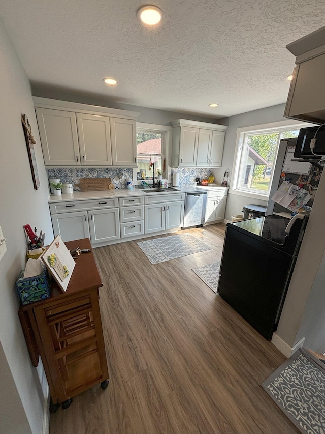 kitchen featuring light wood-type flooring, tasteful backsplash, sink, white cabinets, and stainless steel dishwasher