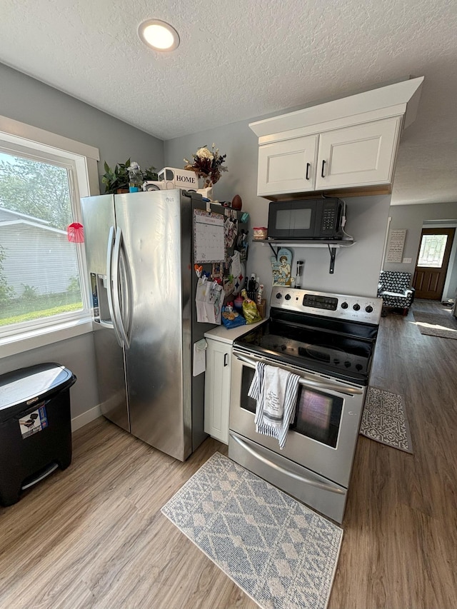 kitchen with appliances with stainless steel finishes, a textured ceiling, white cabinetry, baseboards, and light wood-type flooring