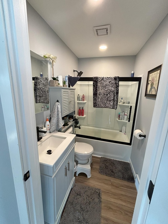 full bathroom featuring hardwood / wood-style floors, combined bath / shower with glass door, vanity, and toilet