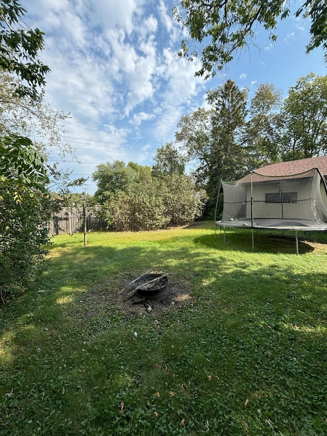 view of yard featuring fence, a trampoline, and a fire pit