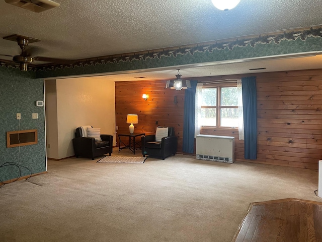 sitting room featuring wooden walls, carpet flooring, heating unit, and a textured ceiling