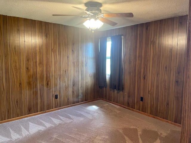 carpeted spare room featuring ceiling fan, wooden walls, and a textured ceiling