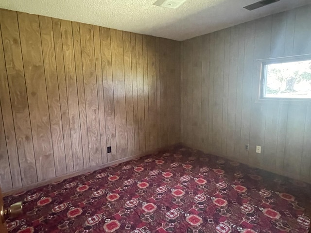 carpeted spare room with wooden walls and a textured ceiling