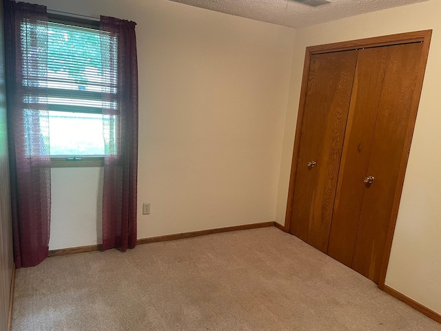 unfurnished bedroom with light colored carpet, a closet, and a textured ceiling