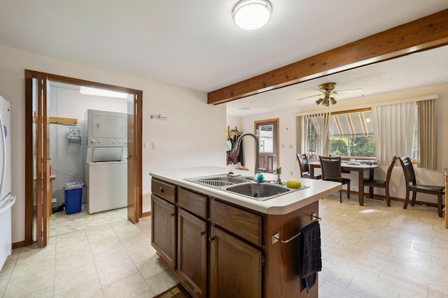 kitchen featuring beam ceiling, stacked washer and dryer, light countertops, a kitchen island with sink, and a sink