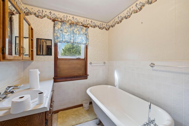 bathroom featuring wallpapered walls, wainscoting, vanity, a freestanding tub, and tile walls