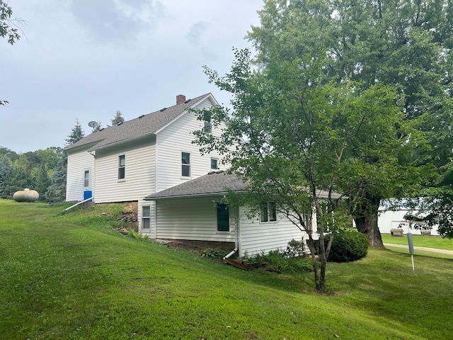 view of side of home featuring a shingled roof, a yard, and a chimney