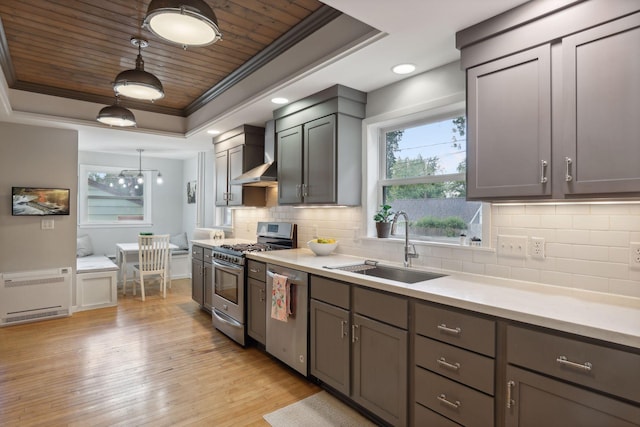 kitchen with appliances with stainless steel finishes, a raised ceiling, sink, and light hardwood / wood-style flooring