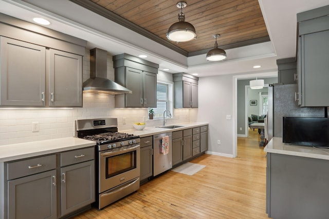 kitchen featuring sink, decorative light fixtures, appliances with stainless steel finishes, a tray ceiling, and wall chimney range hood