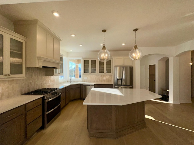 kitchen with a center island, light countertops, appliances with stainless steel finishes, glass insert cabinets, and white cabinets