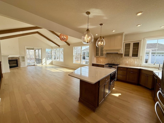 kitchen with vaulted ceiling with beams, open floor plan, light wood finished floors, and a sink