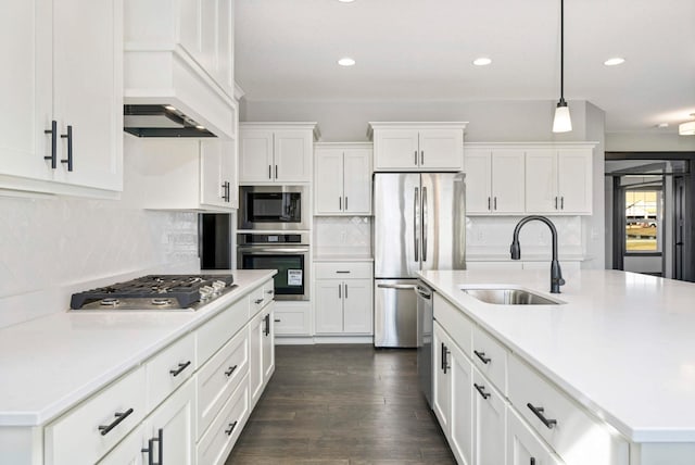 kitchen with stainless steel appliances, a sink, a center island with sink, and white cabinets