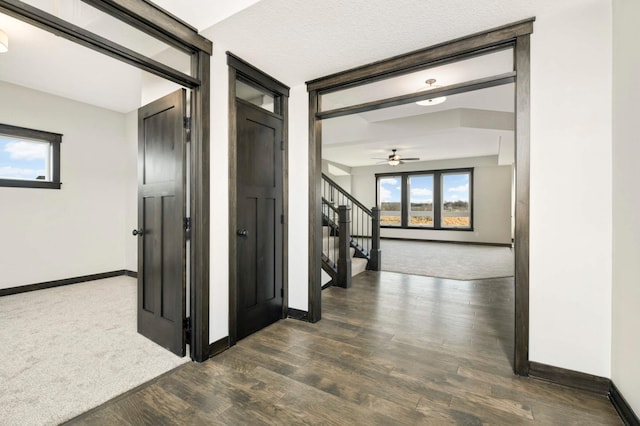 hallway featuring dark wood-style flooring, dark carpet, baseboards, and stairs