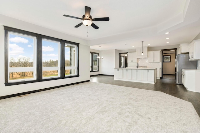 unfurnished living room with plenty of natural light, dark hardwood / wood-style floors, sink, and ceiling fan with notable chandelier