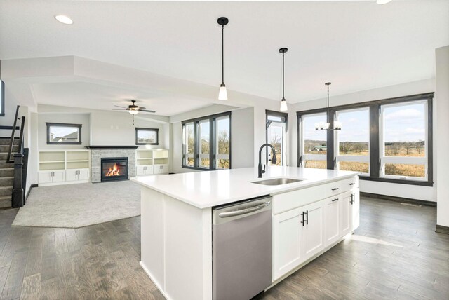 kitchen with stainless steel dishwasher, sink, a stone fireplace, and dark wood-type flooring