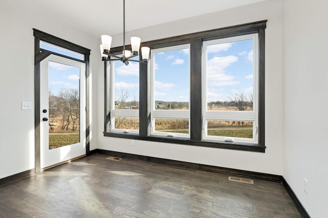 unfurnished dining area with plenty of natural light, dark wood-type flooring, and an inviting chandelier