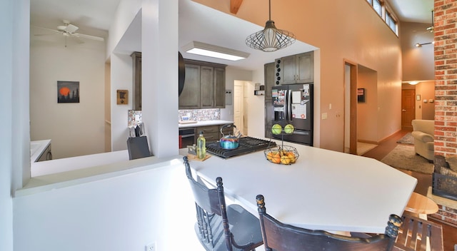 kitchen with ceiling fan, pendant lighting, kitchen peninsula, black refrigerator with ice dispenser, and a towering ceiling