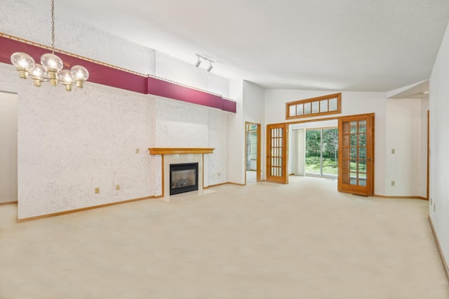 unfurnished living room featuring a tiled fireplace, french doors, vaulted ceiling, and a notable chandelier