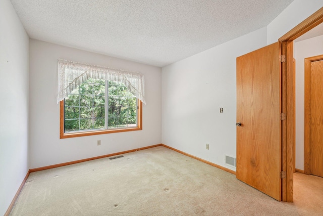 spare room featuring light carpet and a textured ceiling