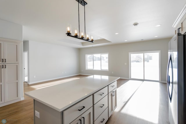 kitchen with stainless steel refrigerator, plenty of natural light, a kitchen island, and light hardwood / wood-style flooring