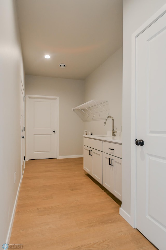 clothes washing area with light hardwood / wood-style floors and sink