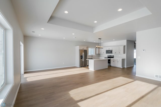 unfurnished living room featuring a tray ceiling, a wealth of natural light, and light wood-type flooring