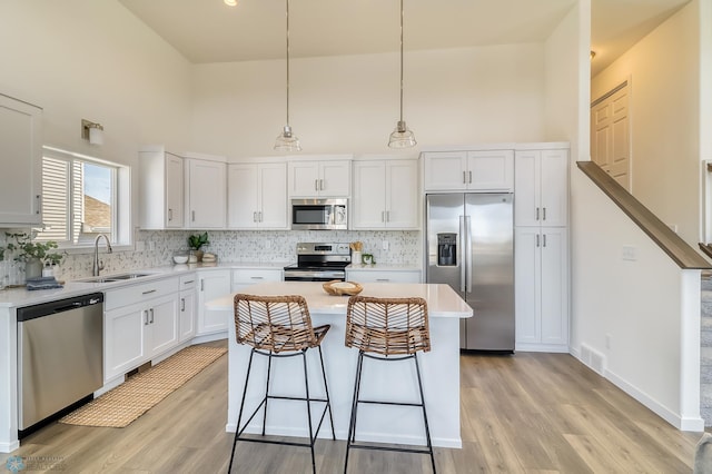 kitchen with light wood-type flooring, stainless steel appliances, a center island, sink, and white cabinets