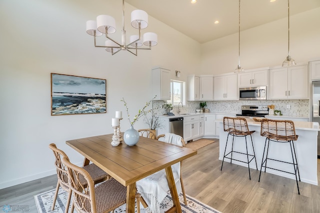 dining room featuring light hardwood / wood-style floors, high vaulted ceiling, a chandelier, and sink