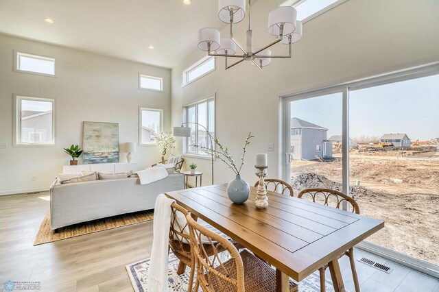 dining area with light hardwood / wood-style flooring, an inviting chandelier, and a towering ceiling