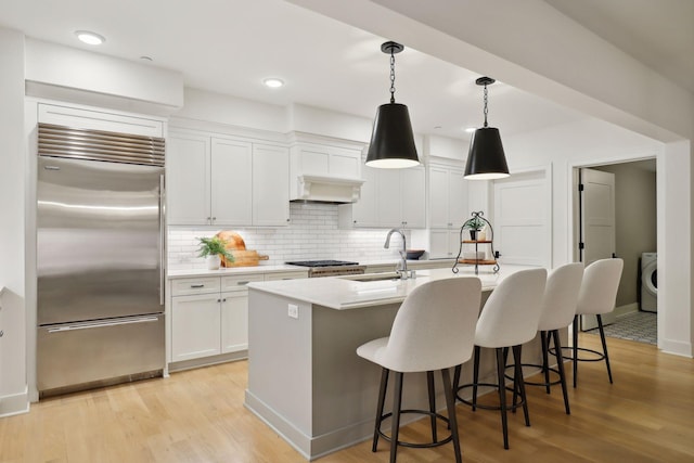 kitchen with light wood-type flooring, stainless steel appliances, sink, and a center island with sink