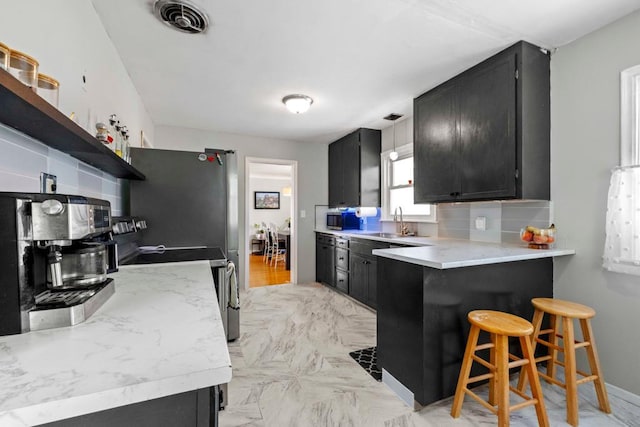 kitchen featuring stainless steel appliances, light countertops, dark cabinetry, and open shelves