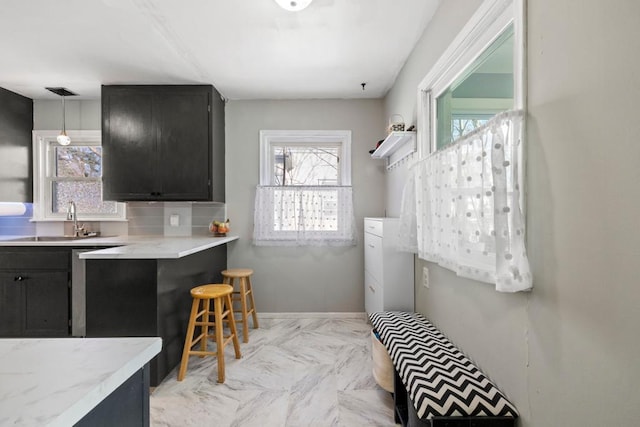 kitchen with a sink, pendant lighting, light countertops, and dark cabinetry