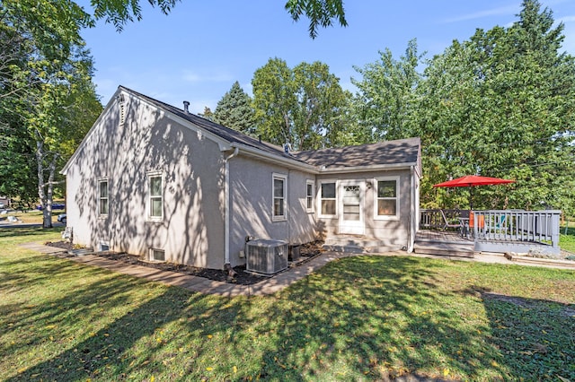 back of property with central AC unit, a deck, a lawn, and stucco siding