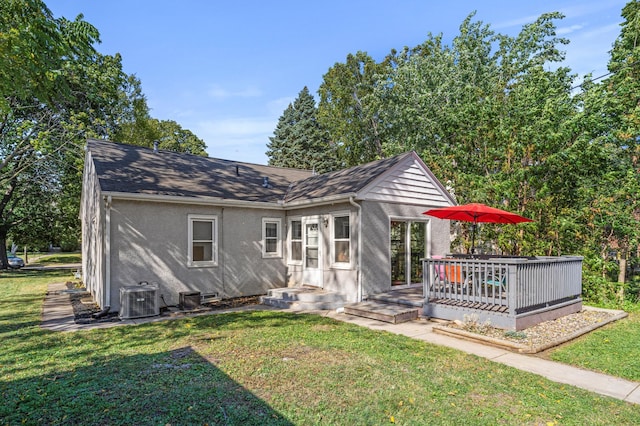 rear view of property featuring stucco siding, a shingled roof, central AC, and a yard