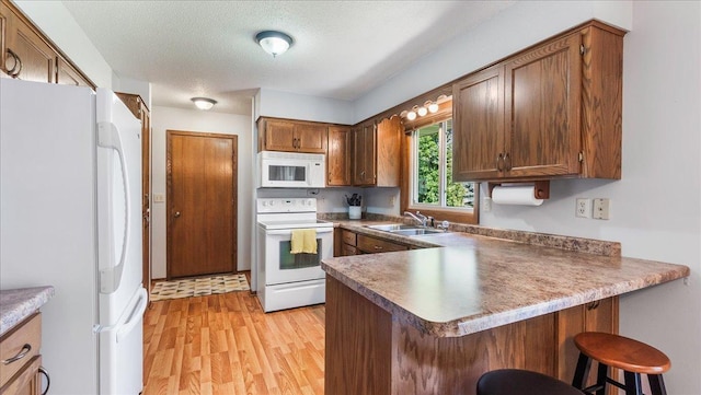 kitchen with brown cabinets, light wood finished floors, a sink, white appliances, and a peninsula