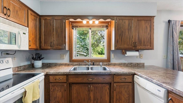 kitchen featuring brown cabinetry, dark countertops, white appliances, and a sink